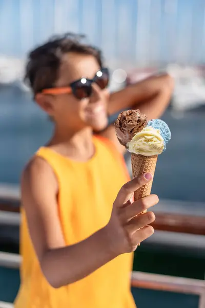 微笑的女孩拿着一个色彩艳丽的冰激凌球 背景是阳光充足的海岸线 免版税图库照片