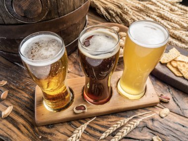 Tahta bira uçuş tahtasının üzerinde üç el yapımı bira. Arka planda bira bardakları, abur cuburlar ve bira fıçıları var..