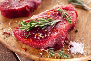 Ahşap tahtanın üzerinde çiğ biftek ve baharat var..