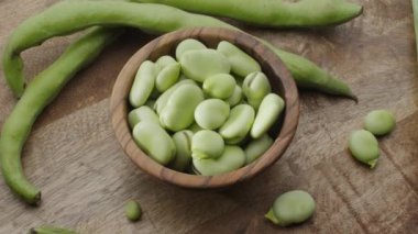 Tahta bir kâse içindeki geniş fasulye ve yanında da ahşap bir masanın üzerindeki geniş fasulye kabukları. Çerçeve videosundaki nesnelerin yavaş dönüşü. 