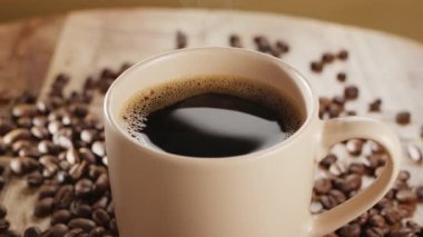 Kahve çekirdekli ahşap bir masanın üzerinde beyaz bir fincan kahve ve yükselen buhar yavaşça döner. Projeleriniz için güzel bir sıcak kahve arka planı..