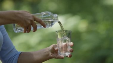 Kadın şişeden bir bardağa saf su döküyor, bulanık yeşil bir arka plan..