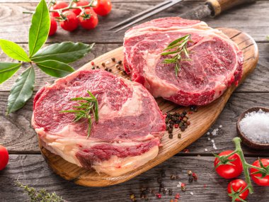 Ahşap tahtanın üzerinde çiğ biftek ve baharat var..