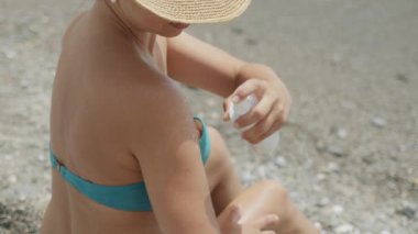 Sahilde otururken omzuna güneş kremi süren bir kadın. Deriyle ilgilenmek ve deriyi güneşten korumak. Sağlıklı tatil kavramı.