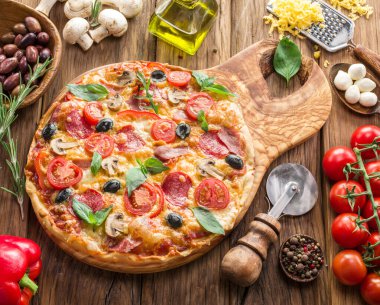 Vişneli domates, salam ve diğer malzemelerle kaplı pizza ahşap masanın üzerinde. Üst görünüm.