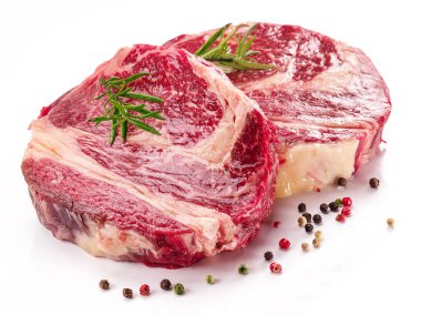 Beyaz arka planda pişmeye hazır baharatlı ve otlu çiğ biftek..