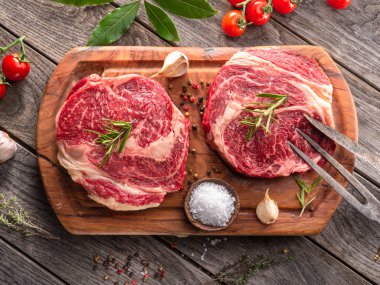 Ahşap tahtanın üzerinde çiğ biftek ve baharat var..