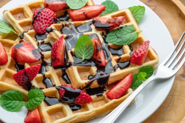 Çikolata soslu Belçika waffleları, çilek dilimleri ve yakın plan nane yaprakları..