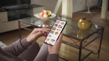  Evde akıllı telefon kullanarak yemek sipariş etmek. Bir Japon restoranının internet menüsünden akıllı telefondan suşi seti seçiyor..