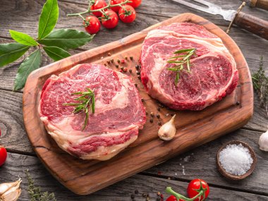 Ahşap tahtanın üzerinde çiğ biftek ve baharat var..