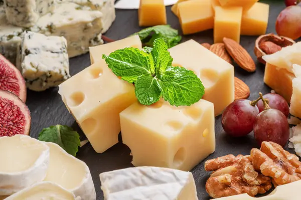 stock image Variety of sliced cheeses with fruits, mint, nuts and cheese cutting knives. Wonderful cheese background for your projects.