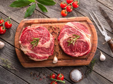 Ahşap tahtanın üzerinde çiğ biftek ve baharat var..