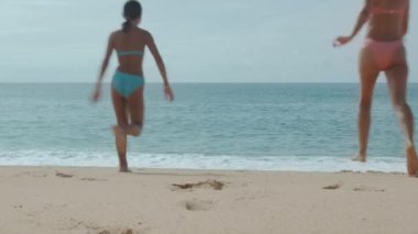 Plajda tatil. Kız ve kadın kameranın önünde koşuyorlar ve okyanusa doğru ilerliyorlar.