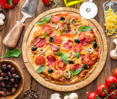 Vişneli domates, salam ve diğer malzemelerle kaplı pizza ahşap masanın üzerinde. Üst görünüm.