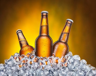 Kahverengi arka planda buz küplerinin içinde üç soğutulmuş bira şişesi..
