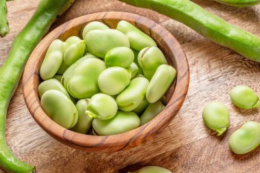 Tahta kasenin içindeki geniş fasulyeler ve ahşap masanın yanındaki geniş fasulye kabukları. Üst görünüm.