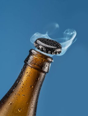 Bira şişesini mavi arka planda açıyorum. Bira şişesinden gaz bulutu yükseliyor..