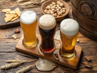 Bira bardağı tutacağında üç bardak bira ve ahşap arka planda bira atıştırmalıkları..