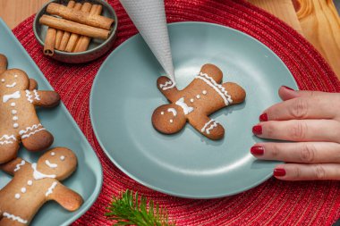 Making Christmas cookies - gingerbread men,  a woman is decorating cookies with royal icing. clipart