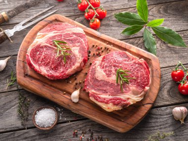 Ahşap tahtanın üzerinde çiğ biftek ve baharat var..