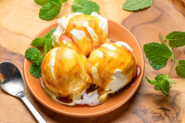 Üç kepçe karamelli vanilyalı dondurma ve ahşap masada taze yeşil nane yaprağı..