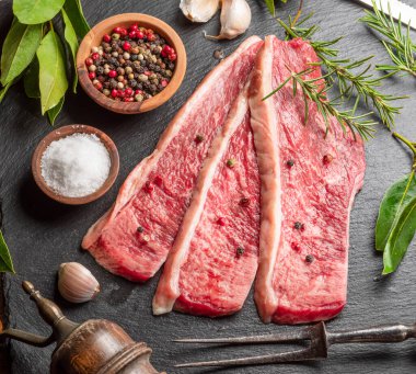 Dilimlenmiş Picanha bifteği, baharat ve otlarla servis edilen gri bir taşın üstünde. Geleneksel Portekiz yemekleri.