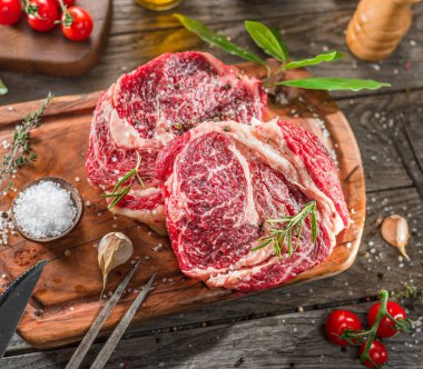 Ahşap tahtanın üzerinde çiğ biftek ve baharat var..