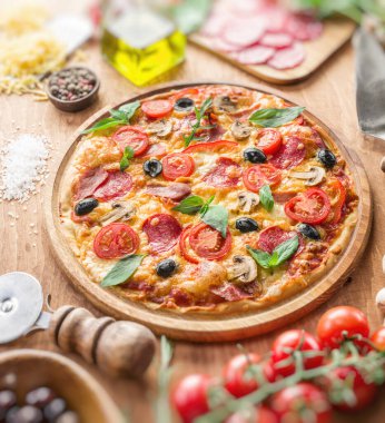 Vişneli domates, salam ve diğer malzemelerle kaplı pizza ahşap masanın üzerinde. Üst görünüm.