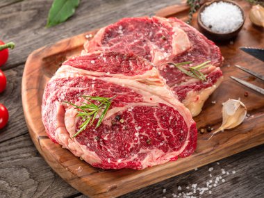 Ahşap tahtanın üzerinde çiğ biftek ve baharat var..