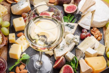 Bir bardak beyaz şarap, çeşitli dilimlenmiş peynirli meyve, nane, fındık ve peynir bıçakları. Projeleriniz için harika şarap ve peynir arka planı..