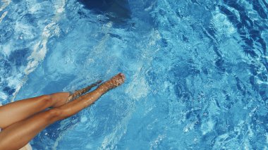 Kadın havuzun kenarında oturuyor. Bacakları suda sallanıyor ve suyu sallıyor. Dalgalar ve küçük dalgalar yaratıyor. Yaz arkaplanı. 