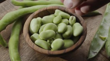 Tahta bir kâse içindeki geniş fasulye ve yanında da ahşap bir masanın üzerindeki geniş fasulye kabukları. Çerçeve videosundaki nesnelerin yavaş dönüşü.