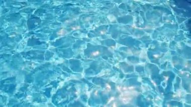 Havuzun suyunda dalgalanmalar, şeffaf, ışıl ışıl, hareketli suyun davetkar yüzeyi, yukarıdan görüş. Yavaş çekim ve döngülü video.