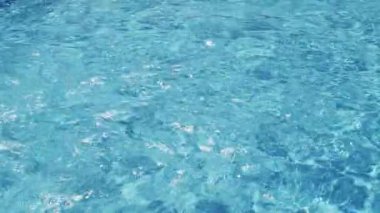 Havuzun suyunda dalgalanmalar, şeffaf, ışıl ışıl, hareketli suyun davetkar yüzeyi, yukarıdan görüş. Yavaş çekim ve döngülü video.
