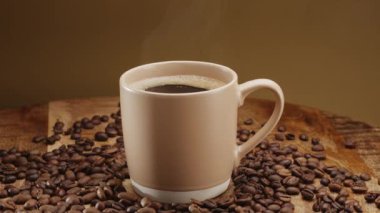 Kahve çekirdekleri olan ahşap bir masada beyaz bir fincan kahve ve yükselen buhar yavaşça döner.. 