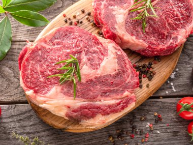 Ahşap tahtanın üzerinde çiğ biftek ve baharat var..