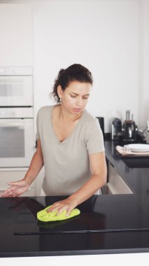 Woman is cleaning the kitchen countertop and electric stove or electric hob.  clipart