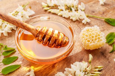 Ahşap kaşığı balla cam kaseye daldırmak, akasya çiçekleri yakındaki ahşap masada. Üst görünüm.