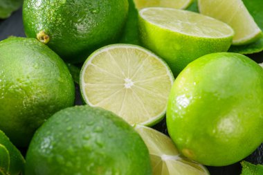 Gri taş bir masada dilimler ve limon yapraklarıyla olgun kireç meyveleri. Projeleriniz için güzel meyve arkaplanı.. 