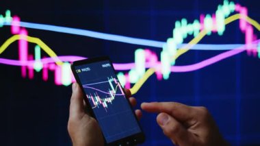 Tüccar veya yatırımcı telefon ve bilgisayar üzerinden borsa veya kripto pazar grafikleri veya grafikleri izliyor veya bakıyor. PS ekranının önündeki grafiklerle el ele tutuşan insanlar.