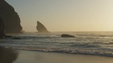 Atlantik Okyanusu 'nun Adraga plajı gün batımında, Sintra Portekiz. Güneş, su yüzeyine parlak bir yol ile yansıdı. Yavaş çekim videosu