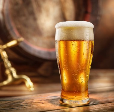 Glass of chilled beer and wooden beer cask on the background.  clipart