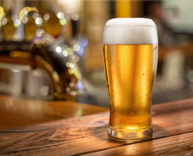 Bir bardak soğuk bira ve arka planda parlak, bulanık bar ekipmanları.. 