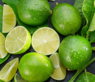 Gri taş bir masada dilimler ve limon yapraklarıyla olgun kireç meyveleri. Projeleriniz için güzel meyve arkaplanı.. 