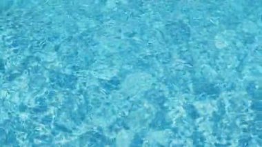 Havuzun suyunda dalgalanmalar, şeffaf, ışıl ışıl, hareketli suyun davetkar yüzeyi, yukarıdan görüş. Yavaş çekim ve döngülü video.