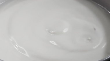 Süt damlası düşer ve su sıçrar; süt yüzeyinde güzel yuvarlak dalgalar bırakır. Yavaş çekim videoyu kapat.
