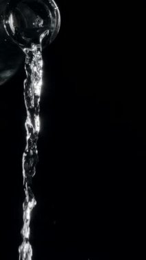 Saf su, siyah arka plandaki cam bir şişeden dökülüyor. Şeffaf su akışı. Yavaş çekim dikey şablonu.