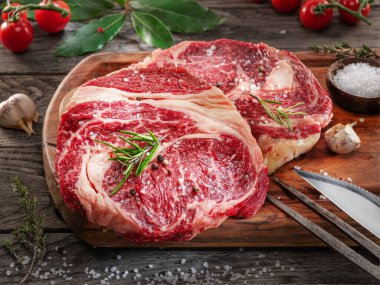 Ahşap tahtanın üzerinde çiğ biftek ve baharat var..