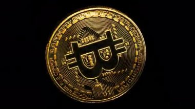 Siyah arka planda Bitcoin logosu etrafında dönen fiziksel altın kaplama sikke. Döngülü video.