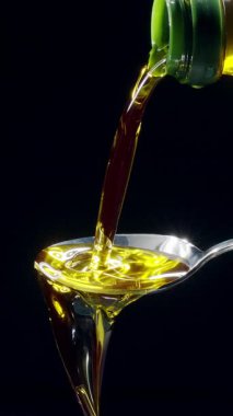 Parlak altın zeytinyağı bir kaşığa dökülüyor ve siyah bir arka planda taşıyor. Yavaş çekim dikey şablonu.